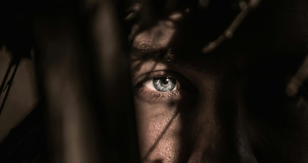 Un homme baigne dans l’ombre, seul son œil est mis en lumière pour imager la thérapie MOSAIC et EMDR à Barcelone.